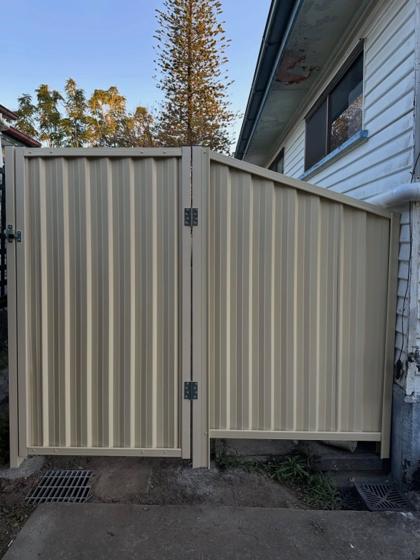 Cream Colorbond side-access gate beside a stepped fence panel by Elite 7 Fencing, Brisbane